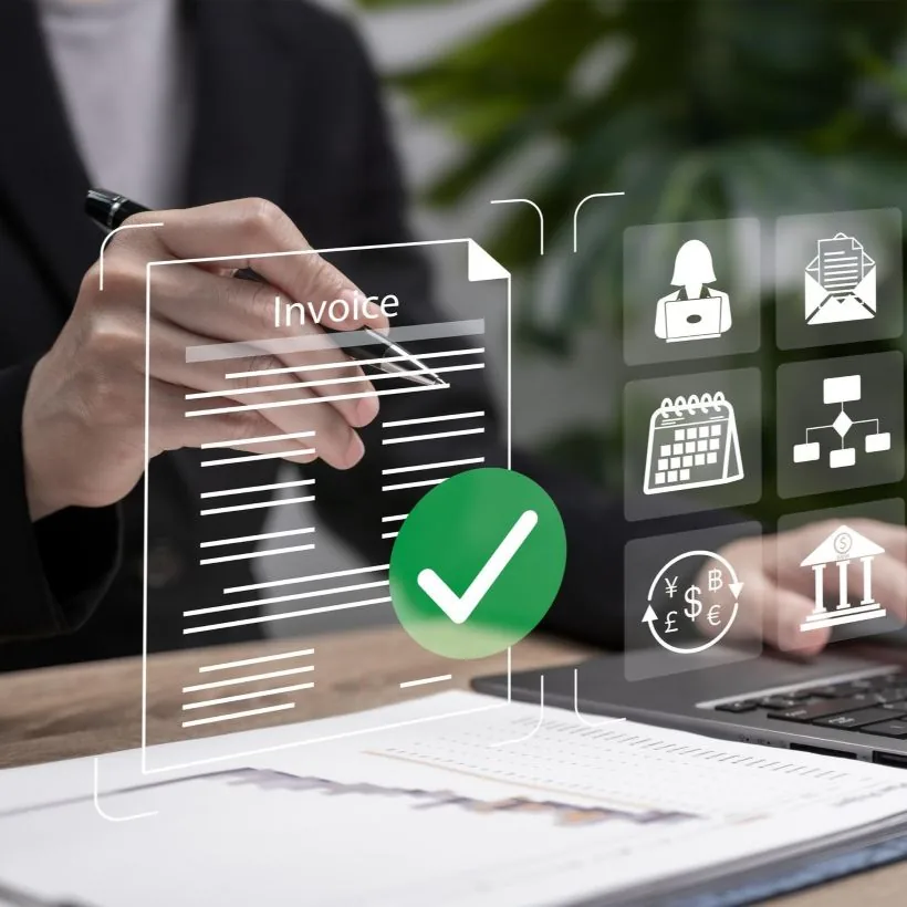 Person in suit holding pen with virtual invoice and financial icons overlay on desk and laptop.